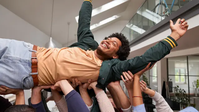 Grupo de associados a levantar outro associado que está a celebrar e a divertir-se. 
