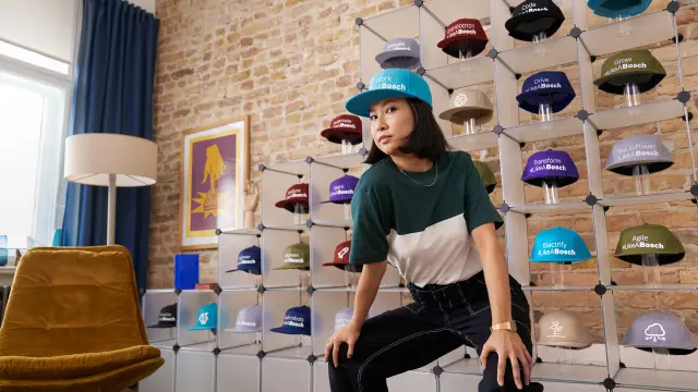 Associada em frente a um expositor cheia de bonés com gravuras relacionadas com a Bosch, como Work #LikeABosch. 