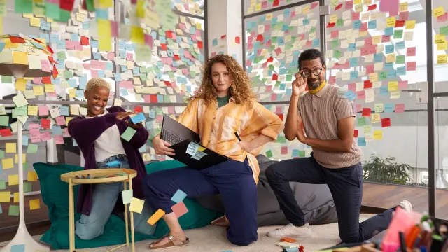 Equipa diversificada de associados divertidos numa sala de reuniões cheia de post-its. 